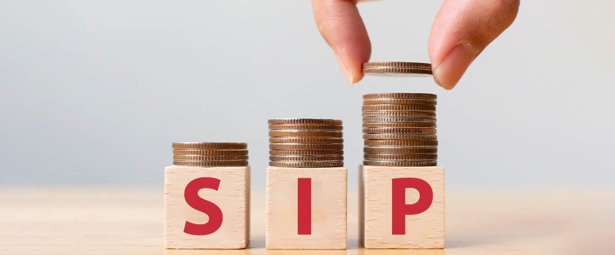 Hand stacking coins on wooden blocks spelling SIP, symbolizing Systematic Investment Plan growth.
