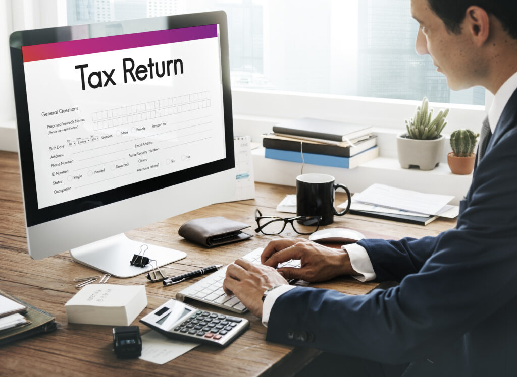 Professional filing an online tax return on a desktop computer with a calculator, documents, and coffee mug on an office desk